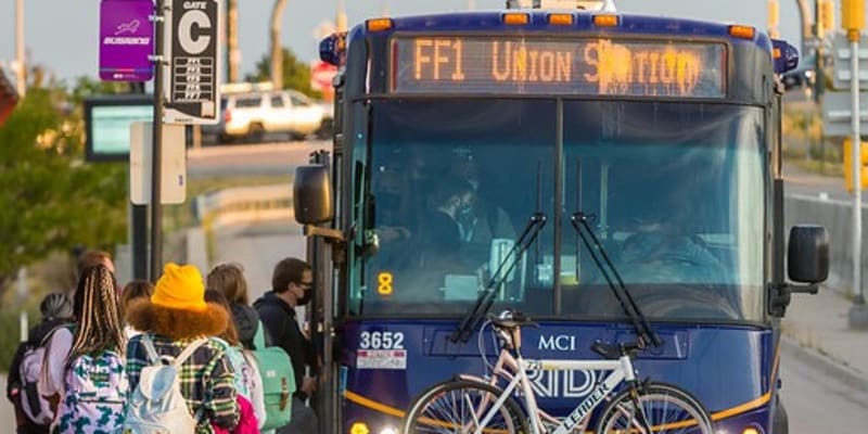 Un grupo de personas espera para subir al FlatIron Flyer en una parada de autobús