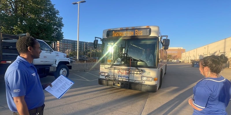 Image of a bus operator trainee in front of a bus with instructor