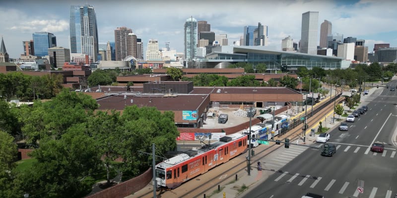 A light rail train near the Colfax at Auraria Station with the city in the background.