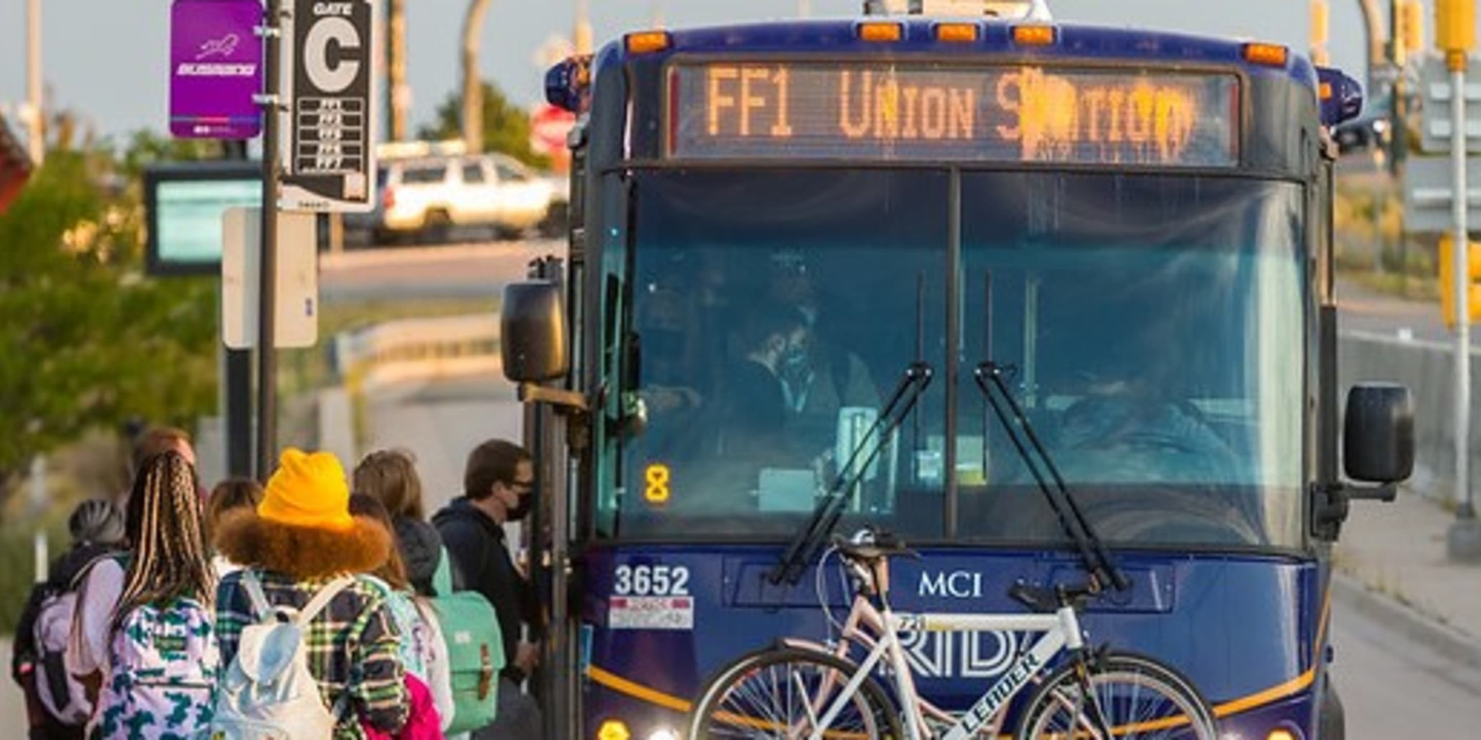 A group of people wait to board the FlatIron Flyer at a bus stop