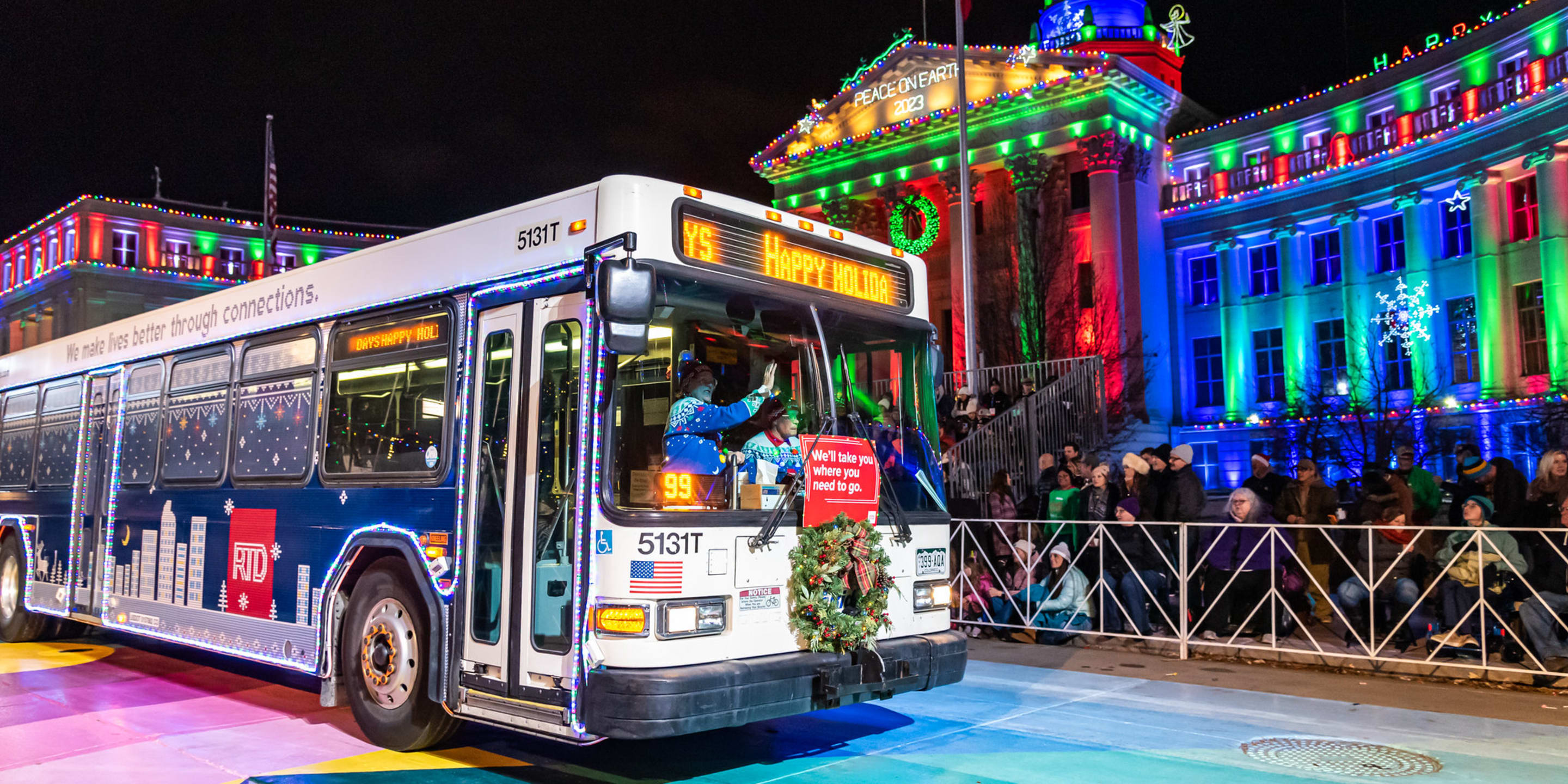 The RTD Christmas bus drives in front of the court house with people watching from the grand stand.